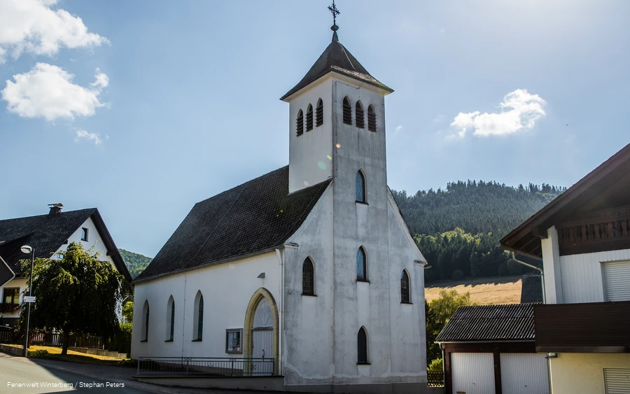 Eine Kirche vor blauem Himmel und Wald.