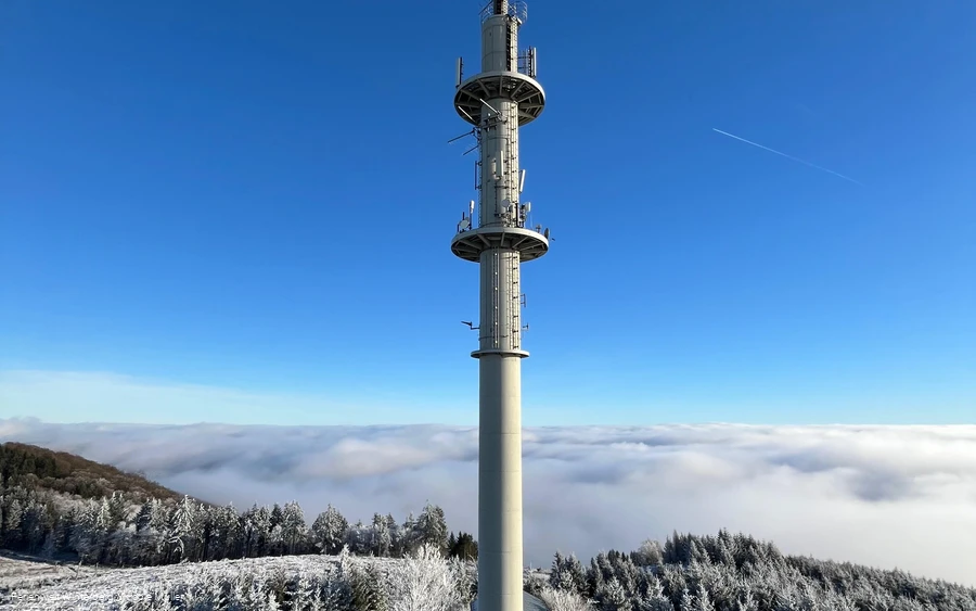 Fernmeldeturm umgeben von Schnee und Nebel vor blauem Himmel. Fernmeldeturm umgeben von Schnee und Nebel vor blauem Himmel.