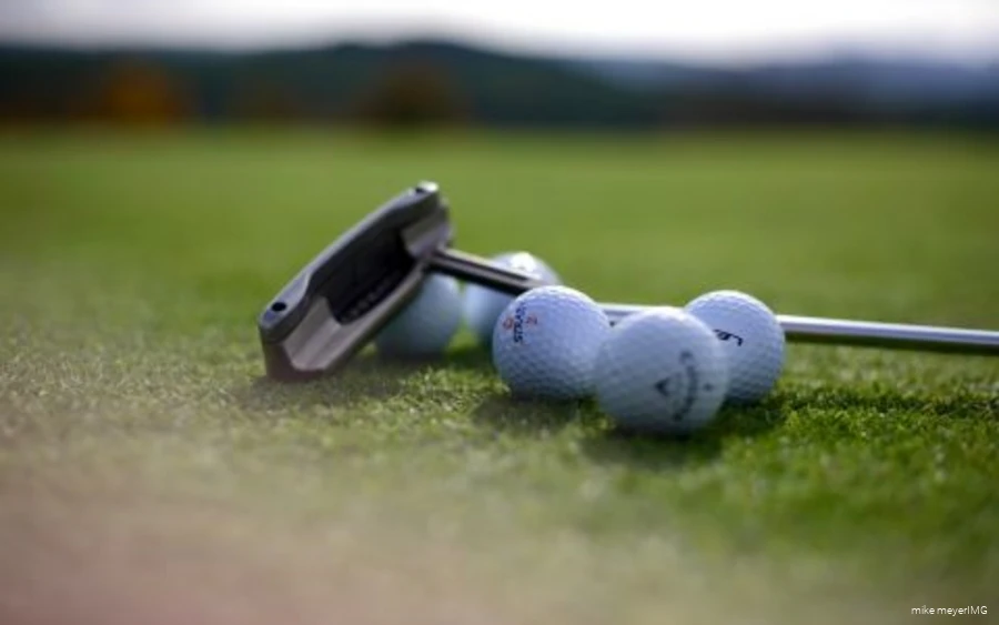 Golf clubs and golf balls are lying on the course.