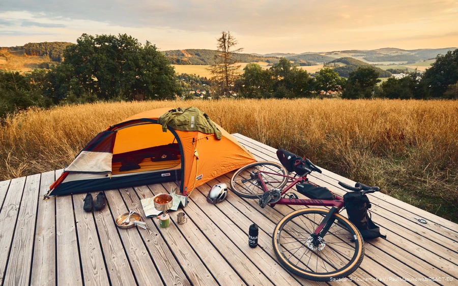 Gravel bike and tent on a trekking platform with a view over the Sauerland landscape