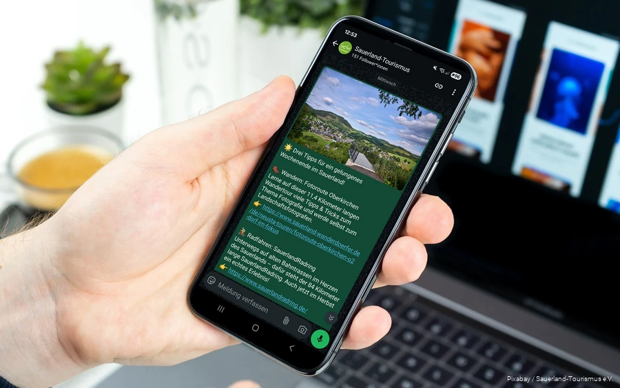 Ein Smartphone wird in der Hand gehalten. Auf dem Bildschirm sieht man einen Post im neuen WhatsApp-Kanal des Sauerland-Tourismus.