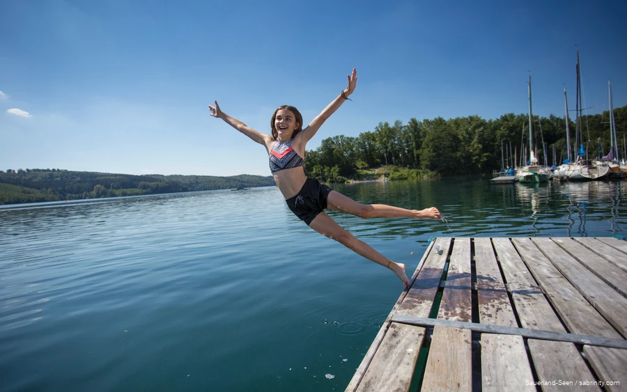 Een meisje springt van de steiger in het meer.