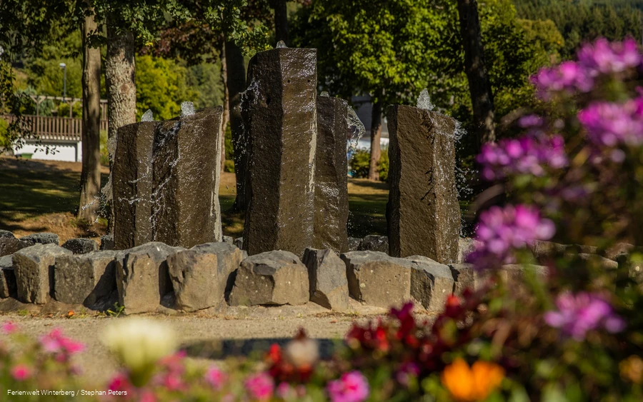 Ein steinerner Brunnen mit vier großen Steinsäulen, aus denen Wasser sprudelt.