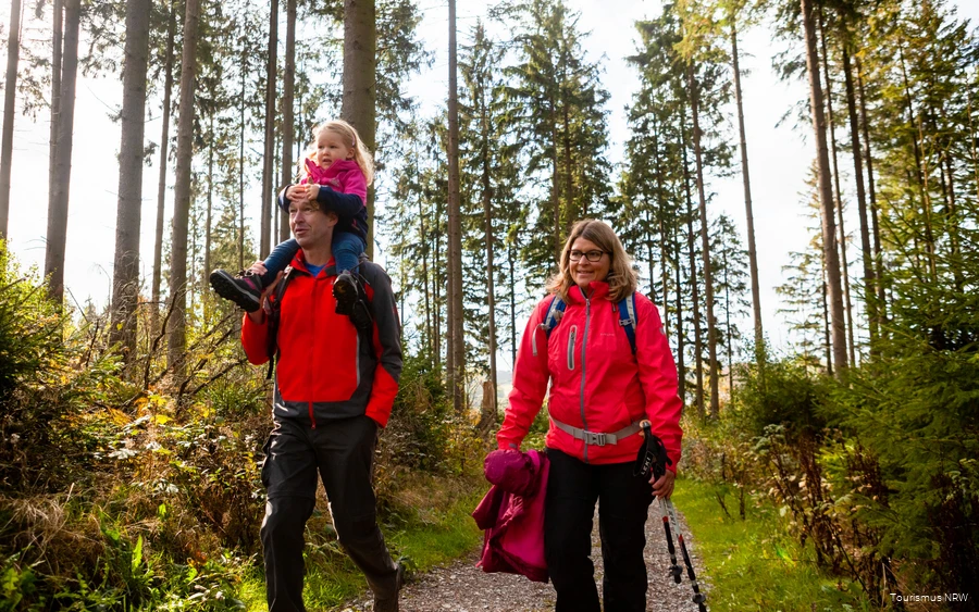 A family on a hike through the autumnal Sauerland landscape. The father carries his daughter on his shoulders.