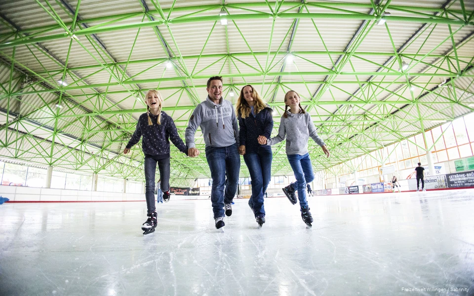 Vater, Mutter und zwei Töchter fahren Hand-in-Hand auf Schlittschuhen.