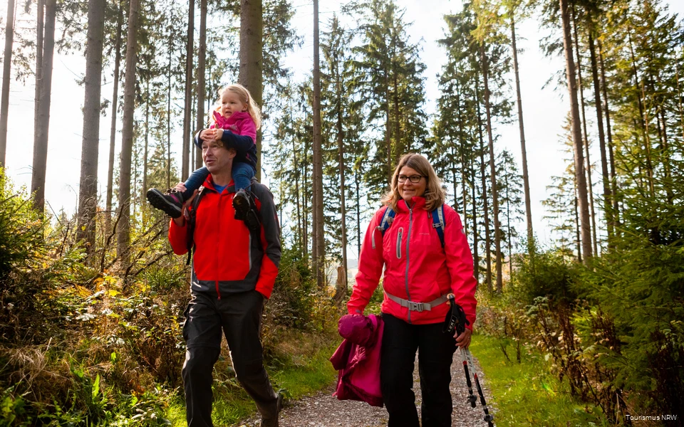 Een gezin tijdens een wandeling door het herfstige landschap van Sauerland. De vader draagt zijn dochter op zijn schouders.