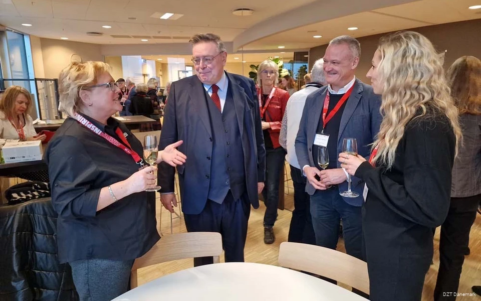 Twee vrouwen praten met twee mannen. Ze hebben champagneglazen in hun handen en ID-kaarten om hun nek.