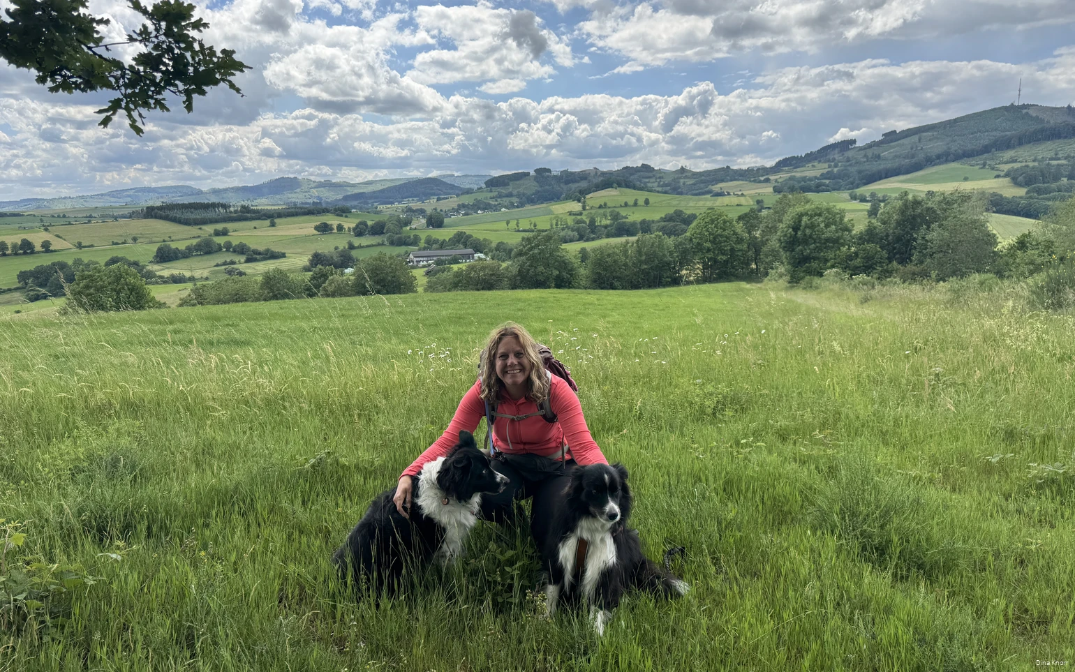 Bloggerin Dina Knorr posiert mit ihren beiden Hunden vor der grünen Sauerländer Landschaft auf einer ihrer Wanderrunden.