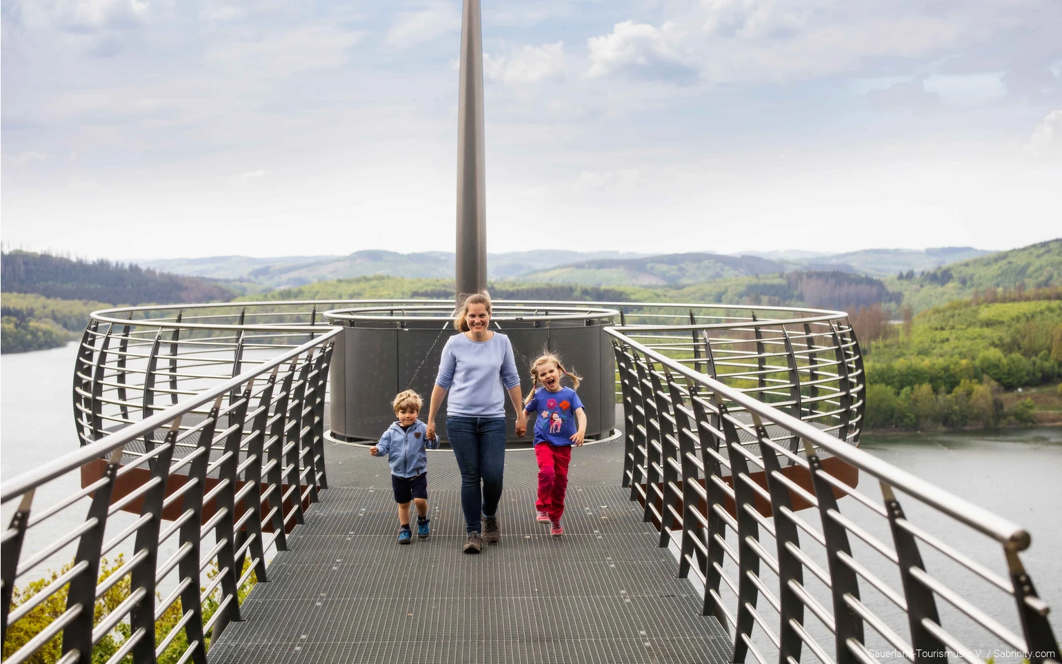 Eine Mutter läuft mit zwei Kindern an der Hand über den Skywalk Biggeblick.