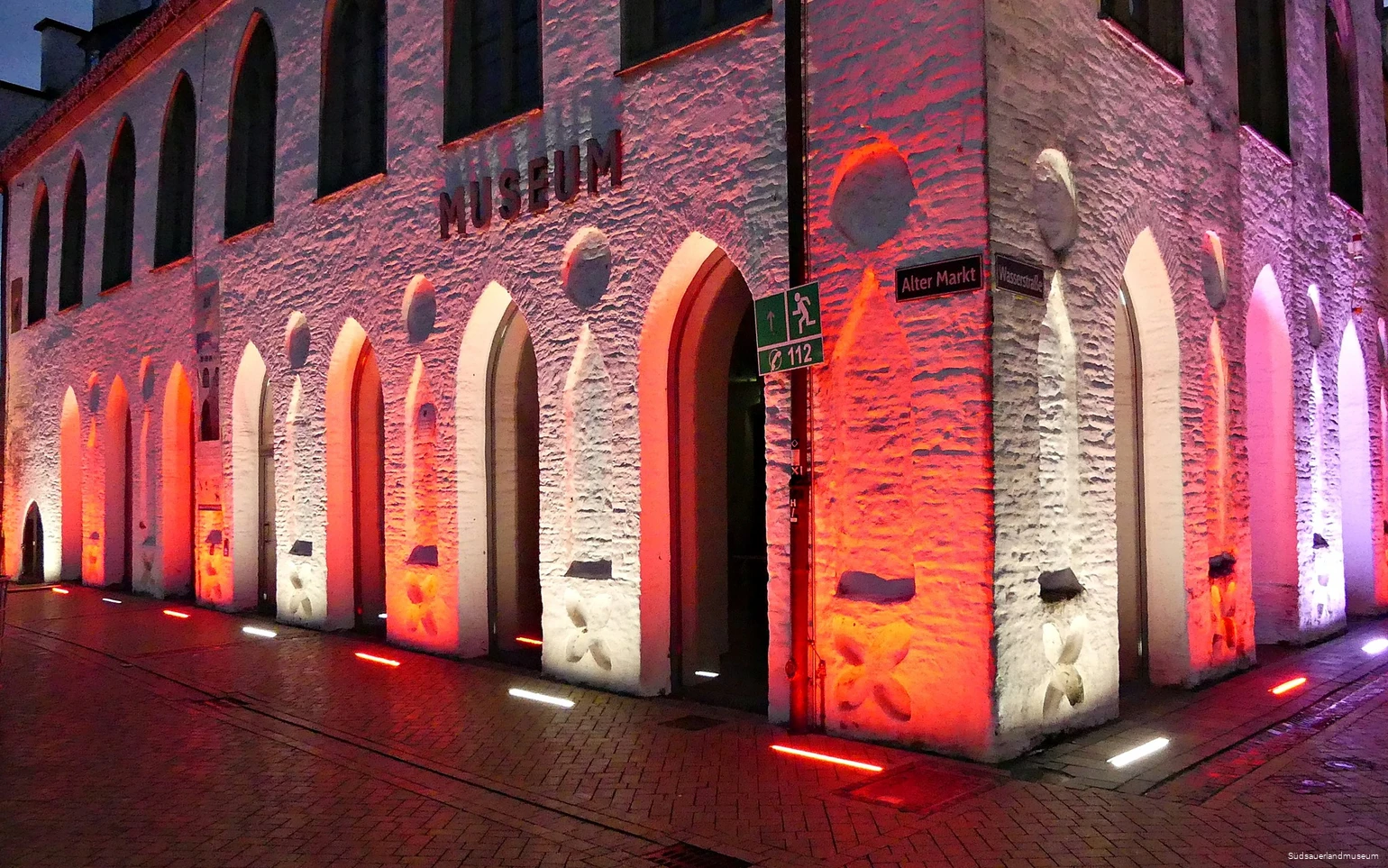Beleuchtete Fassade des Südsauerlandmuseums in rot und weiß. An der Mauer steht die Aufschrift Museum.