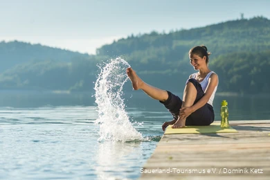Een vrouw zit op een steiger aan het Hennesee meer en plonst met water.