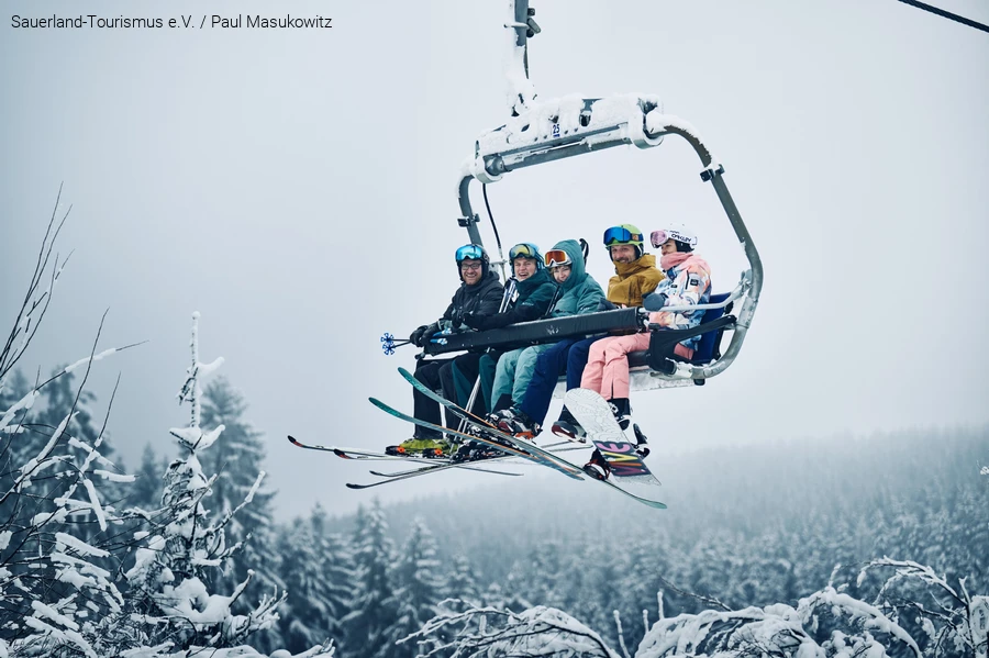 A cheerful group of winter sports enthusiasts is sitting in the chairlift.
