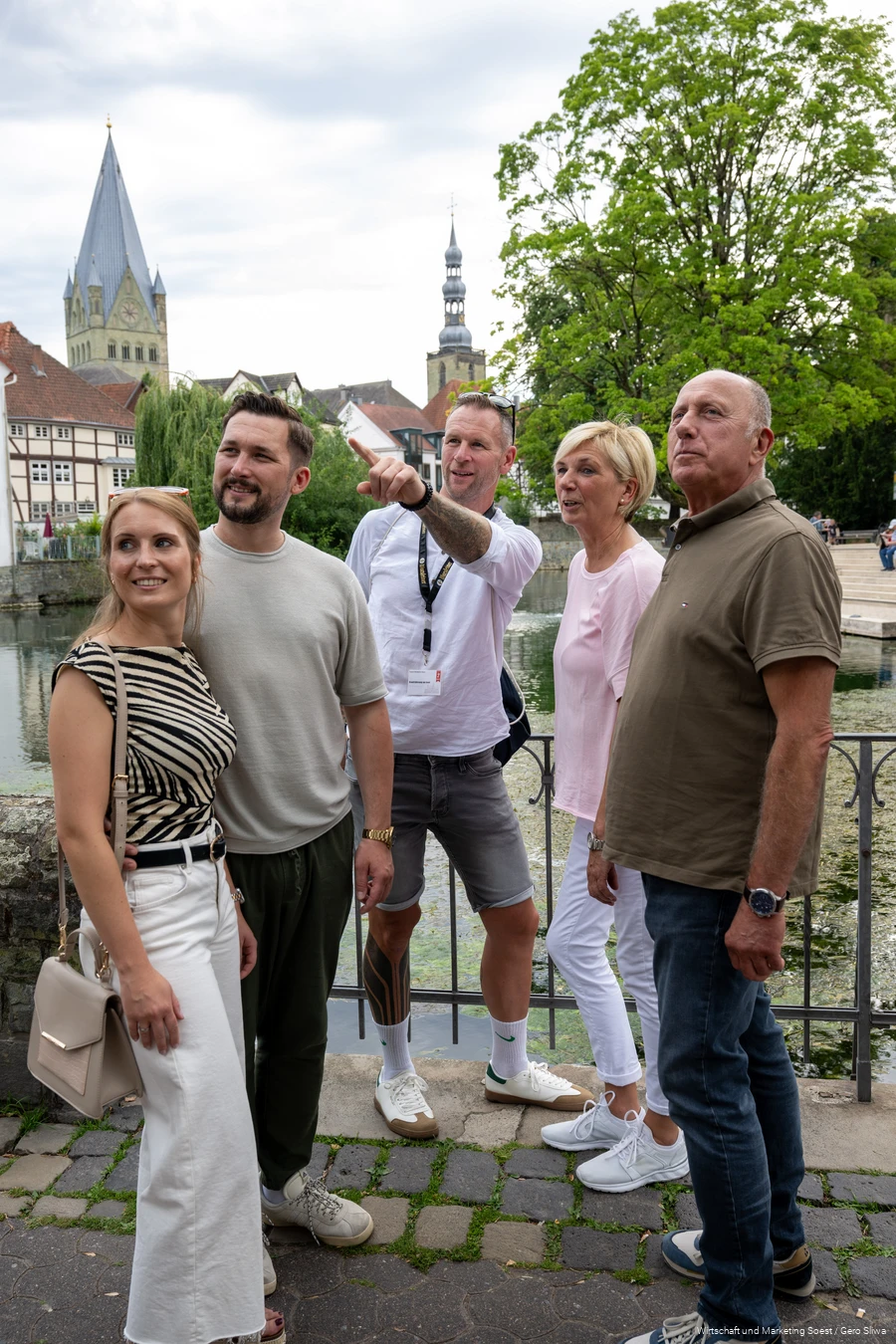 Gruppe steht mit Guide am Großen Teich in Soest mit Kirchtürmen und Fachwerkhäusern im Hintergrund. Der Guide zeigt auf etwas.