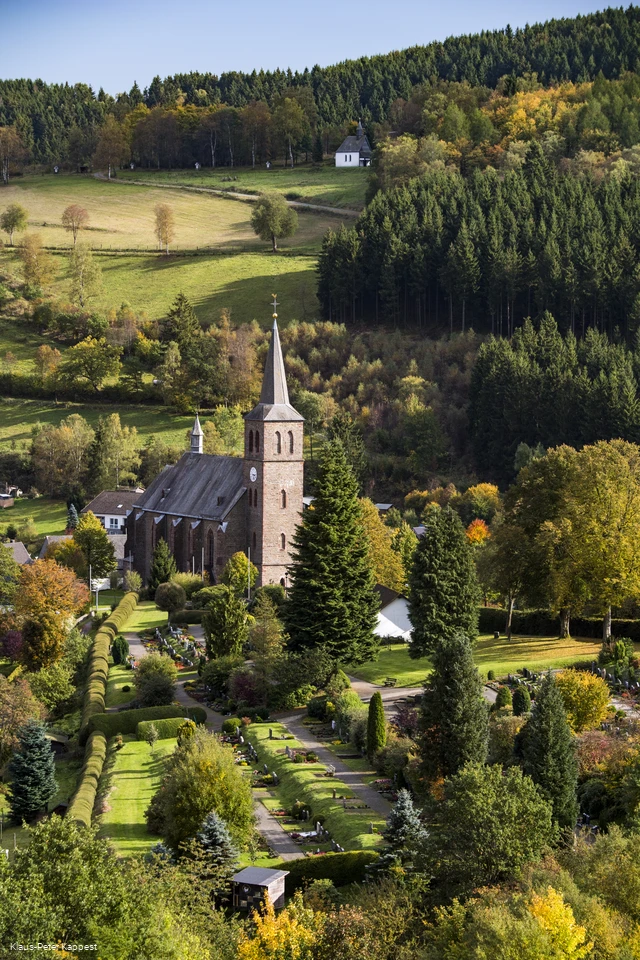 Drohnenaufnahmeeiner Kirche umgeben von Wiesen und Wäldern.