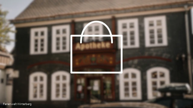 Verschwommenes Bild einer Apotheke mit der Zeichnung eines Koffers im Vordergrund. Dieses Bild dient als Symbolbild für Apotheken.