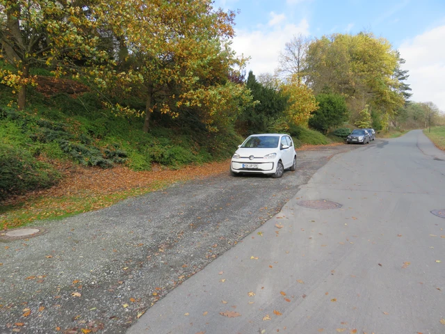 Ein Schotterparkplatz neben einer Straße mit drei parkenden Autos.