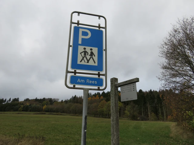 Parkplatzschild mit weißem P auf blauem Grund und darunter zwei Männchen mit einem Wanderstock und der Aufschrift Am Rees.