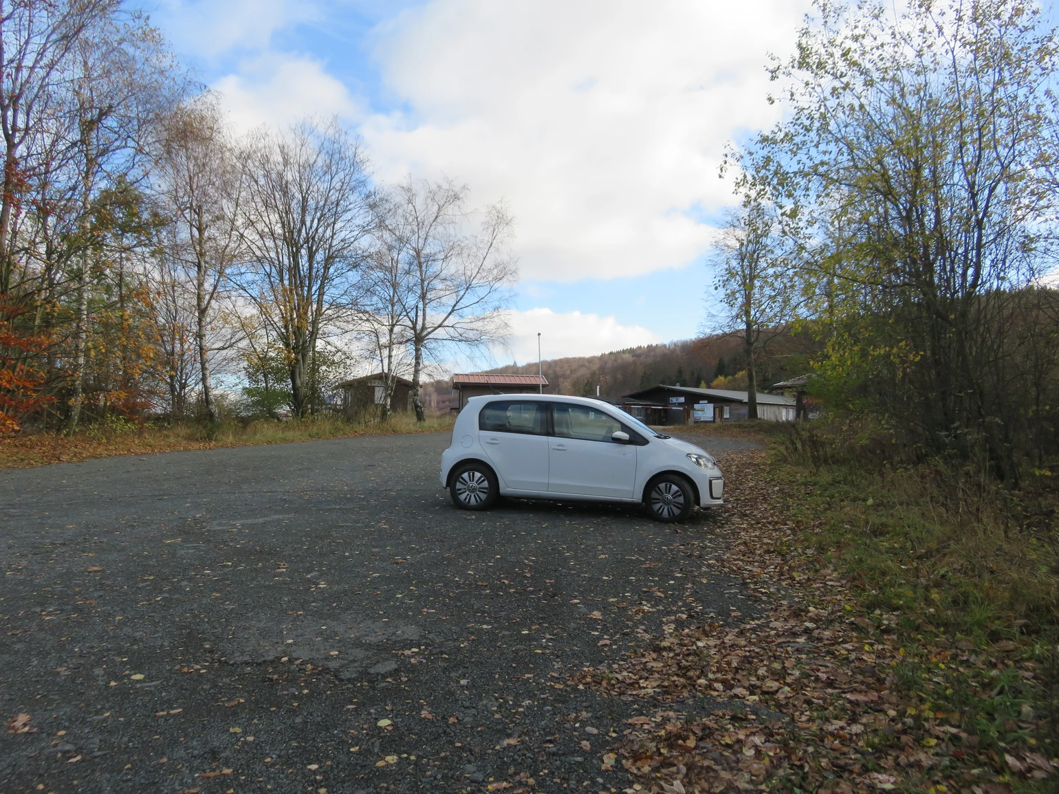 Ein kleines weißes Auto parkt auf einem Parkplatz am Wegesrand.