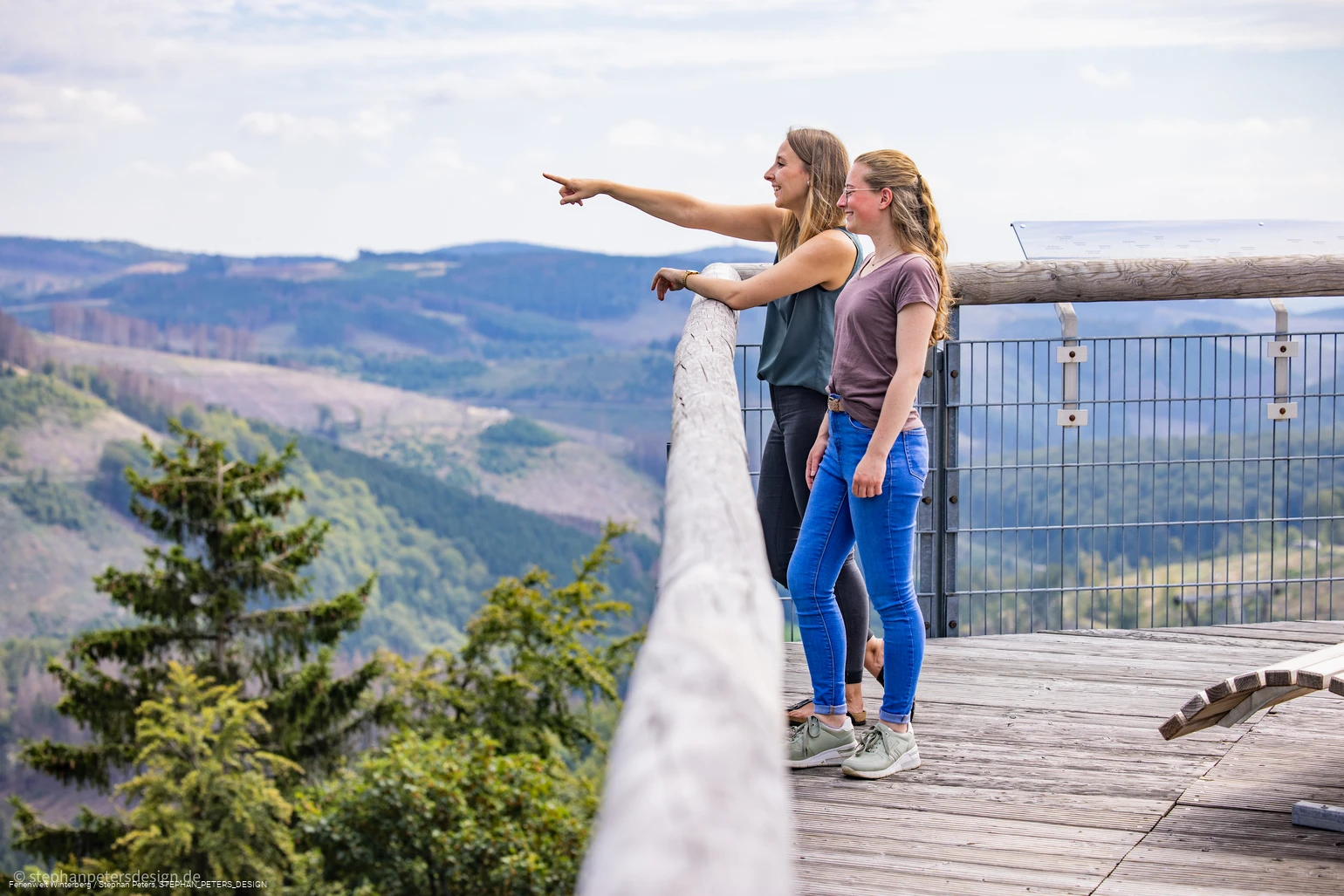 Zwei Frauen stehen auf einer hohen Brücke und blicken in die Ferne.