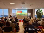 Eine größere Gruppe Menschen schaut auf eine Präsentation. Daneben stehen zwei Frauen, die vortragen.