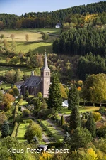 Drohnenaufnahmeeiner Kirche umgeben von Wiesen und Wäldern.