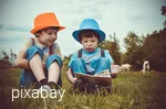 Two boys are sitting in a cow meadow reading a book.