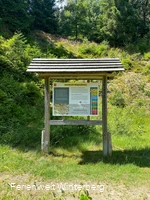 Informationstafel zum Steinbruch Wagenschmier mit grün bewachsenem Steinbruch im Hintergrund.