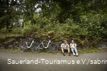 A couple of cyclists take a break at the side of the road.