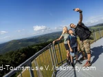 Eltern mit Sohn stehen auf einem Aussichtspunkt und machen ein Selfie mit dem Ausblick auf die sauerländer Berge im Hintergrund.