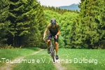 Tätowierter Mann auf einem Gravelbike von vorne. Er fährt einen kleinen Pfad umgeben von Nadelbäumen hoch.