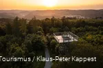 Blick von oben auf den Turm. Im Hintergrund geht die Sonne unter und man sieht verschiedene Ortschaften
