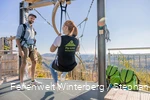 Eine Frau sitzt in einem Sitzgurt, welcher an einer Metallschiene hängt auf einer Startplattform.