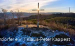 Landscape shot of the summit cross on the Olsberg at sunrise. There is a thin layer of snow.