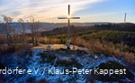 Landscape shot of the summit cross on the Olsberg at sunrise. There is a thin layer of snow.