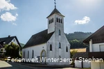 Eine Kirche vor blauem Himmel und Wald.