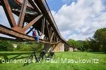 Pärchen sitzt auf dem Träger einer Brücke unter ihnen zwei E-Bikes