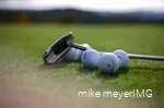 Golf clubs and golf balls are lying on the course.