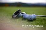 Golf clubs and golf balls are lying on the course.