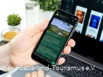 Ein Smartphone wird in der Hand gehalten. Auf dem Bildschirm sieht man einen Post im neuen WhatsApp-Kanal des Sauerland-Tourismus.