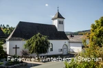 Eine Kirche vor blauem Himmel und einem Baum im Vordergrund.