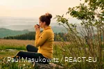 A hiker enjoys her break with a cup of coffee and a view over the landscape.