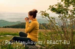 A hiker enjoys her break with a cup of coffee and a view over the landscape.