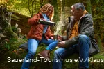 Een koppel neemt een koffiepauze op een boomstam in het bos.