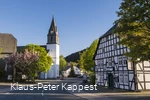 Eine Kirche an einer Straße mit einem Fachwerkhaus im Vordergrund.