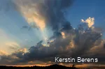 Dunkle Wolken am Abendhimmel mit orangenem Horizont und Sonnenstrahlen, die hinter den Wolken hervorkommen.