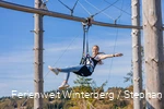 Eine Frau hängt an einem Sitzgurt an einer Metallschiene und breitet die Arme aus.