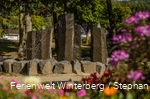 Ein steinerner Brunnen mit vier großen Steinsäulen, aus denen Wasser sprudelt.