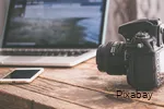 Zicht op een tafel met laptop, smartphone en spiegelreflexcamera.