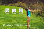 A man doing archery in the meadow.
