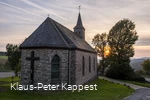 Eine steinerne Kapelle umgeben von einer grünen Wioese mit der untergehenden Sonne im Hintergrund.